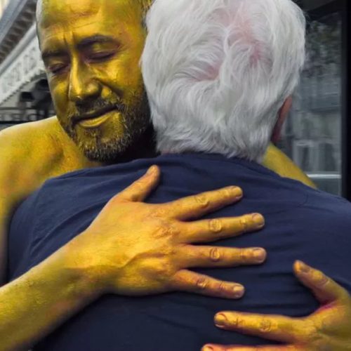 un uomo colorato di oro abbraccia Alejandro Jodorowsky