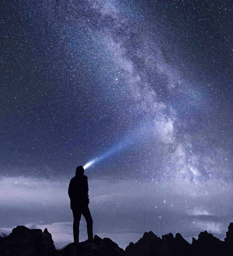 uomo con lampada frontale contempla il cielo notturno