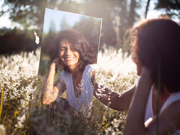 donna si guarda nello specchio in un campo di fiori: l'irretimento nelle costellazioni familiari è visto come il riflesso della vita di un antenato sulla nostra