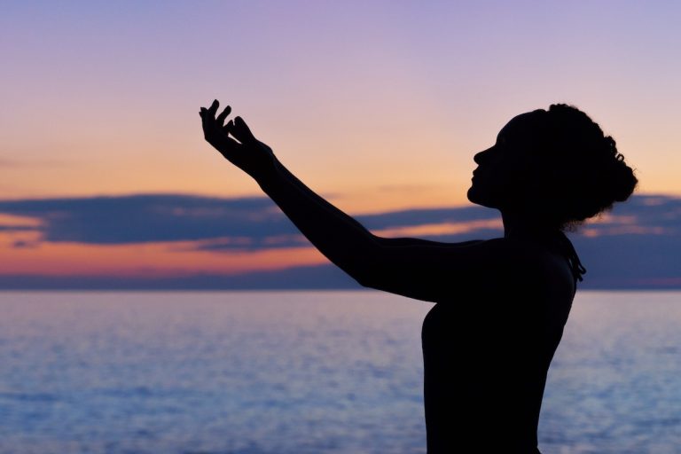 donna prega con il mare e il tramonto sullo sfondo