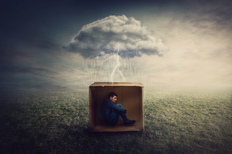 uomo chiuso in una scatola di cartone sotto una nuvola dalla quale piove. Le forme pensiero negativo sono come una nuvola che rimane su di noi
