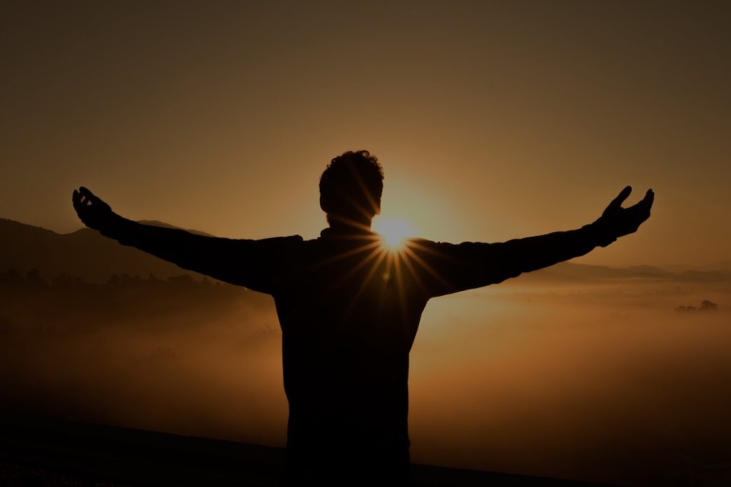 uomo apre le braccia di fronte al sole: le forme pensiero si generano dalla mente