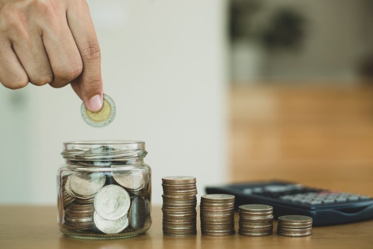 una mano impila monete fuori e dentro un vaso di vetro: insieme al crollo del mito del posto fisso è cambiata la visione del guadagnare e dei soldi