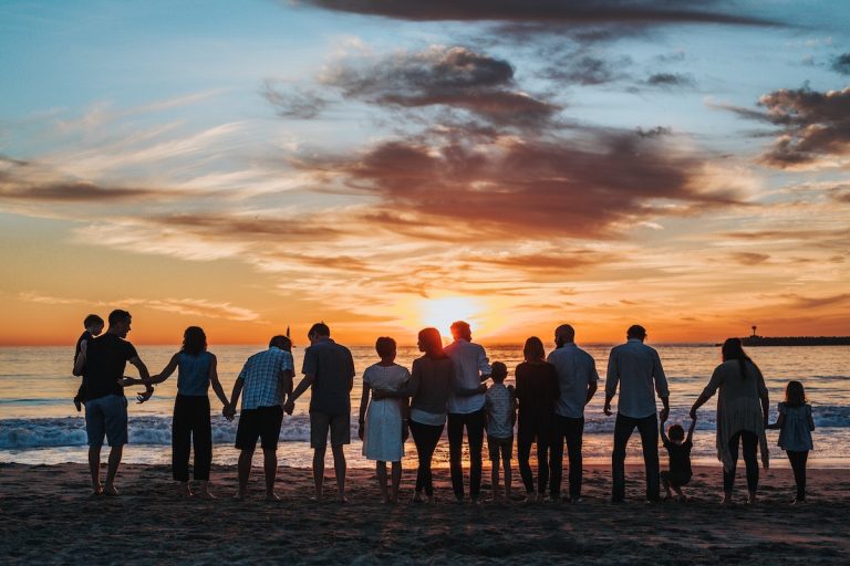 una grande famiglia sulla spiaggia guarda verso il mare al tramonto. Perché le costellazioni familiari si chiamano così visto che si parla di famiglia?