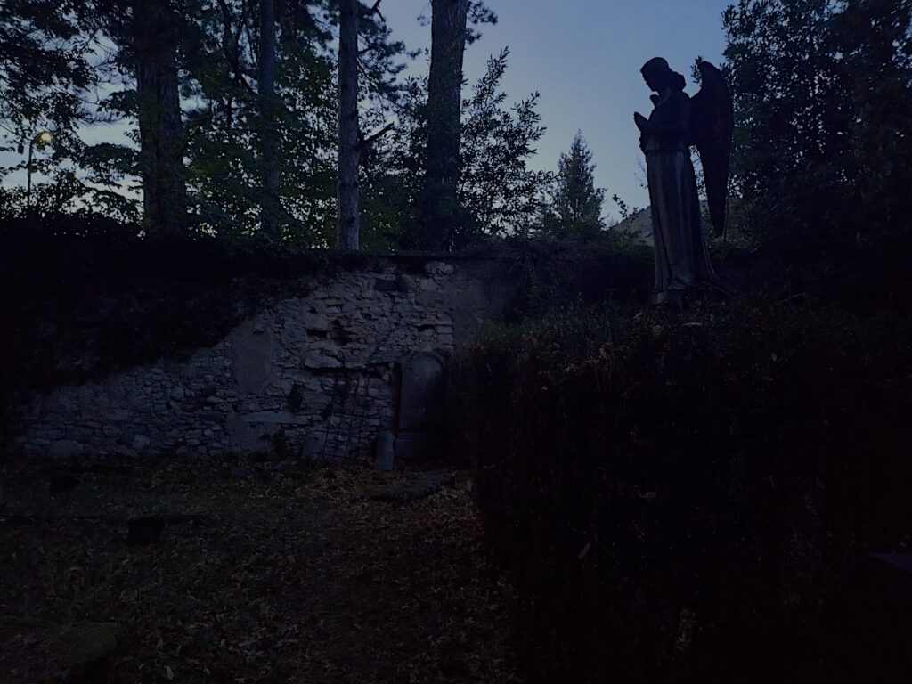 foto all'interno di un cimitero monumentale la sera con vista di una statua di angelo