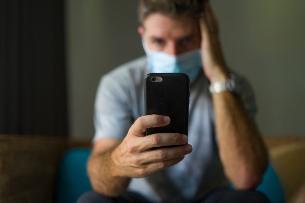 following online news on covid-19 virus pandemic – man with face mask in home quarantine lockdown checking internet information on the contagious disease worried uomo preoccupato con mascherina guarda il cellulare: le costellazioni familiari di fine anno aiutano a lasciare alle spalle questi anni difficili