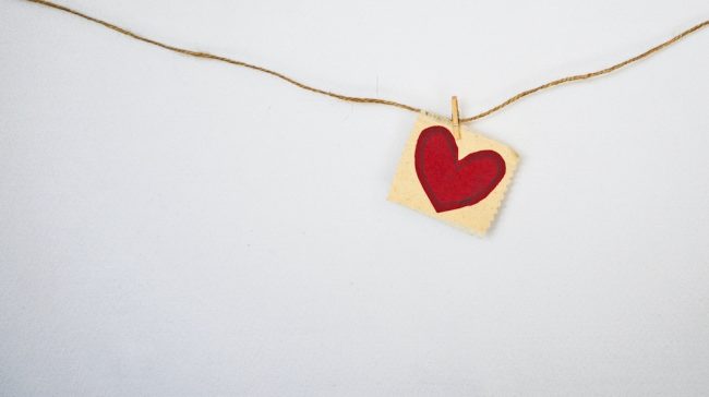 cuore rosso colorato sopra un foglio appeso con una molletta a un filo