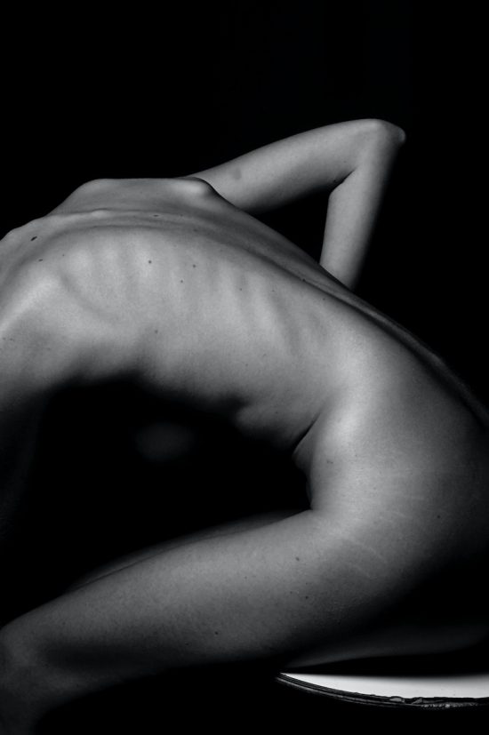 schiena di donna nuda flessa su di sé con la mano posta su un fianco. Il mal di schiena può essere un fastidio invalidante