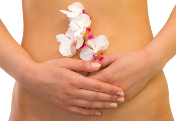 Picture of a woman hand holding an orchid in front of her abdomen