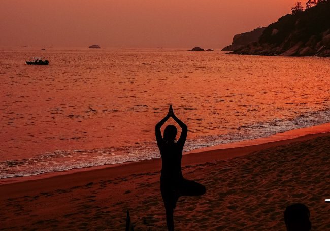 donna pratica yoga in spiaggia al tramonto: rappresenta l'equilibrio nella domanda: preferisci sapere o essere?