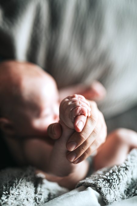 bambina neonata stringe un dito adulto: i nonni nelle costellazioni familiari spesso sostituiscono il ruolo di genitori assenti