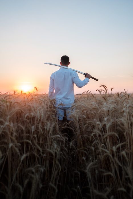 uomo appoggia una spada sulle spalle in un campo di grano rimanendo in presenza